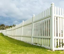 A long white picket fence bordering a grassy lawn.