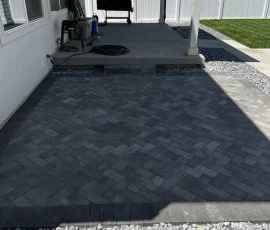 A herringbone-patterned paver patio adjacent to a raised concrete porch with a grill.