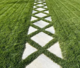 A diamond-patterned stone walkway set into a grassy lawn.