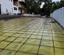 Construction site showing a large rectangular area covered in yellow vapor barrier and metal rebar grid.