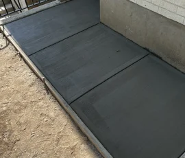 Newly poured concrete walkway next to a white brick wall and a black metal railing.