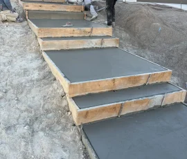 Three workers smoothing wet concrete steps framed with wooden boards outside a house.