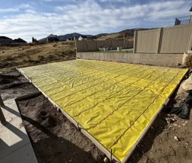 A rectangular concrete patio foundation covered with a yellow vapor barrier and metal rebar grid.