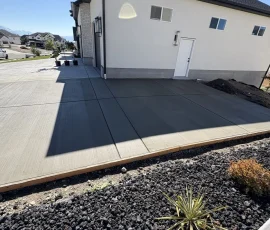 Newly poured concrete patio adjacent to the side of a house with black lava rock landscaping in the foreground.