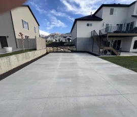 A large, newly poured concrete driveway between two residential houses with a mountain view in the background.