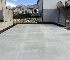 A newly poured concrete patio in a backyard with a stone retaining wall and mountain views.