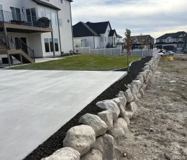 A large stone retaining wall bordering a concrete patio and a grassy backyard in a suburban neighborhood.