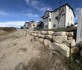 Large stone retaining wall in front of multi-story suburban houses.