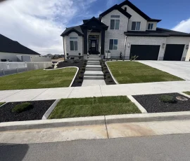 Two-story house with a white brick exterior, black roof, and front lawn with landscaped mulch beds.
