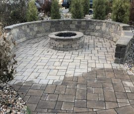 A stone fire pit surrounded by a curved stone wall on a paved patio.