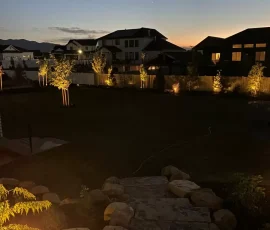 A backyard at dusk with lit stone steps in the foreground and silhouettes of houses against the horizon.