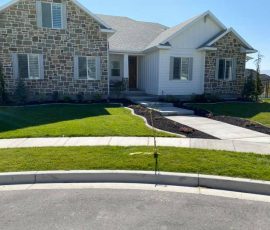 A one-story house with stone and white vertical siding, a front walkway, and a landscaped lawn.