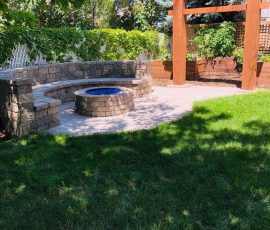 A curved stone bench surrounds a circular fire pit in a backyard with a wooden pergola.