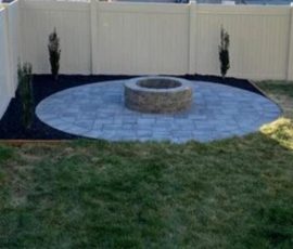 Circular paver patio with a stone fire pit in a fenced backyard.