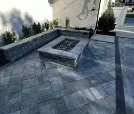 A stone fire pit surrounded by a stone bench on a paved patio.