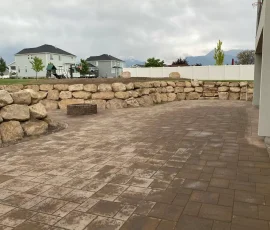 A stone paver patio with a low stone retaining wall, a stone fire pit, and a small staircase.