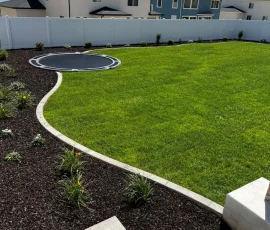 Backyard with a green lawn, mulch garden beds, and an in-ground trampoline.