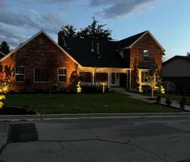 A brick house at twilight with glowing landscape lighting illuminating the lawn and exterior.