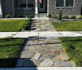 A stone walkway leads from the street to the front porch of a stone-faced house.